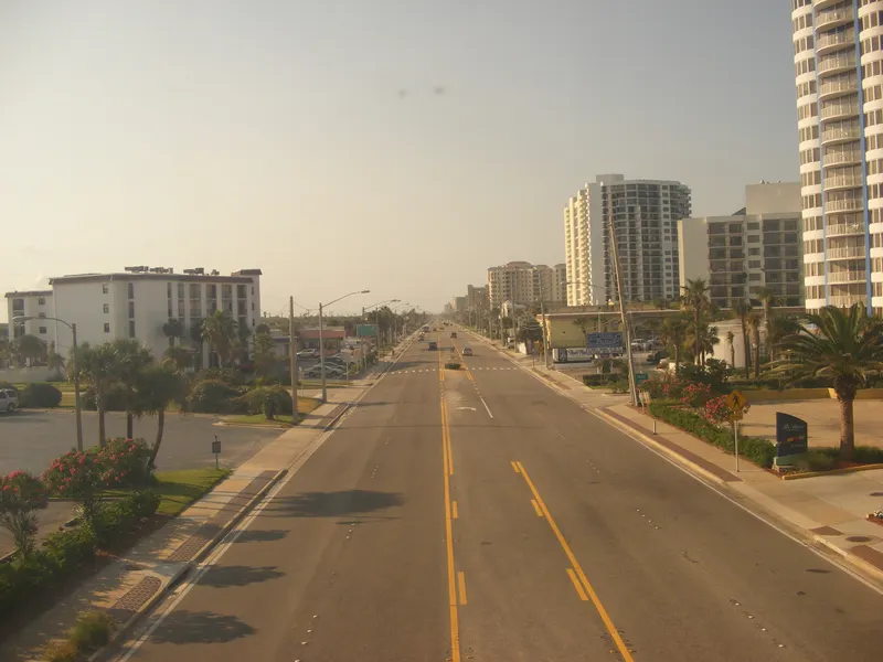 Four-lane Atlantic Avenue (A1A) running north between palms and oceanfront high-rise condos, seen from above