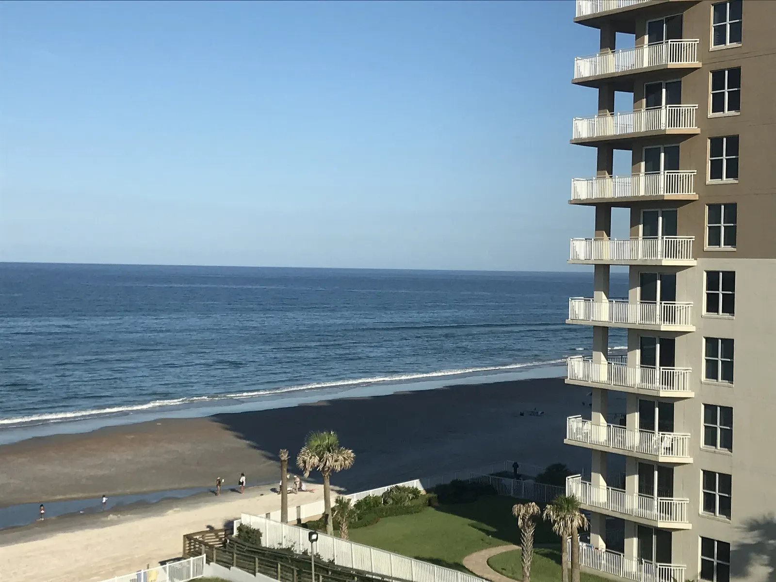 Oceanfront condo tower with white balconies beside a wide beach and the Atlantic, seen from an upper floor