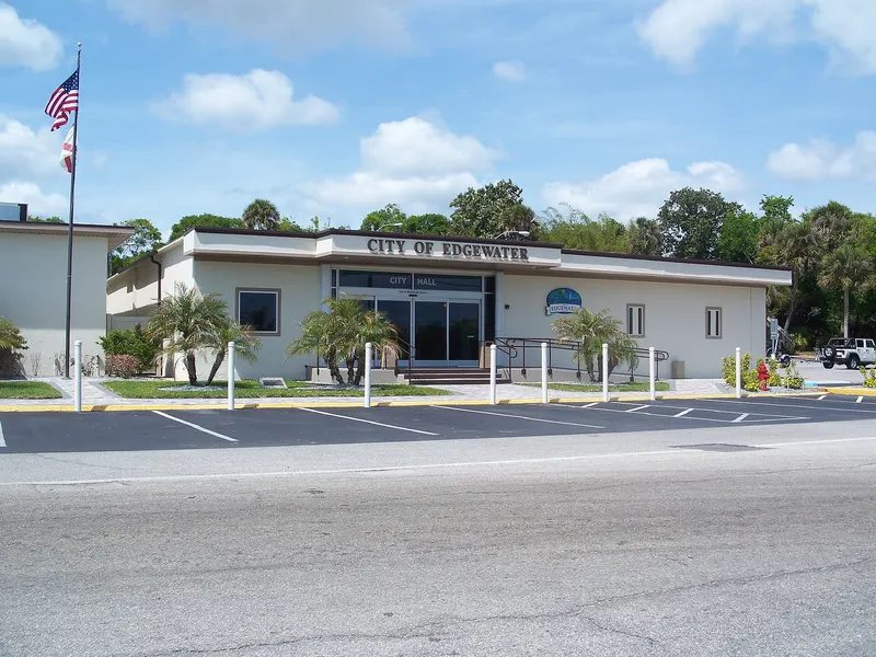 Single-storey City of Edgewater city hall with palms, flagpole and an empty parking lot in front