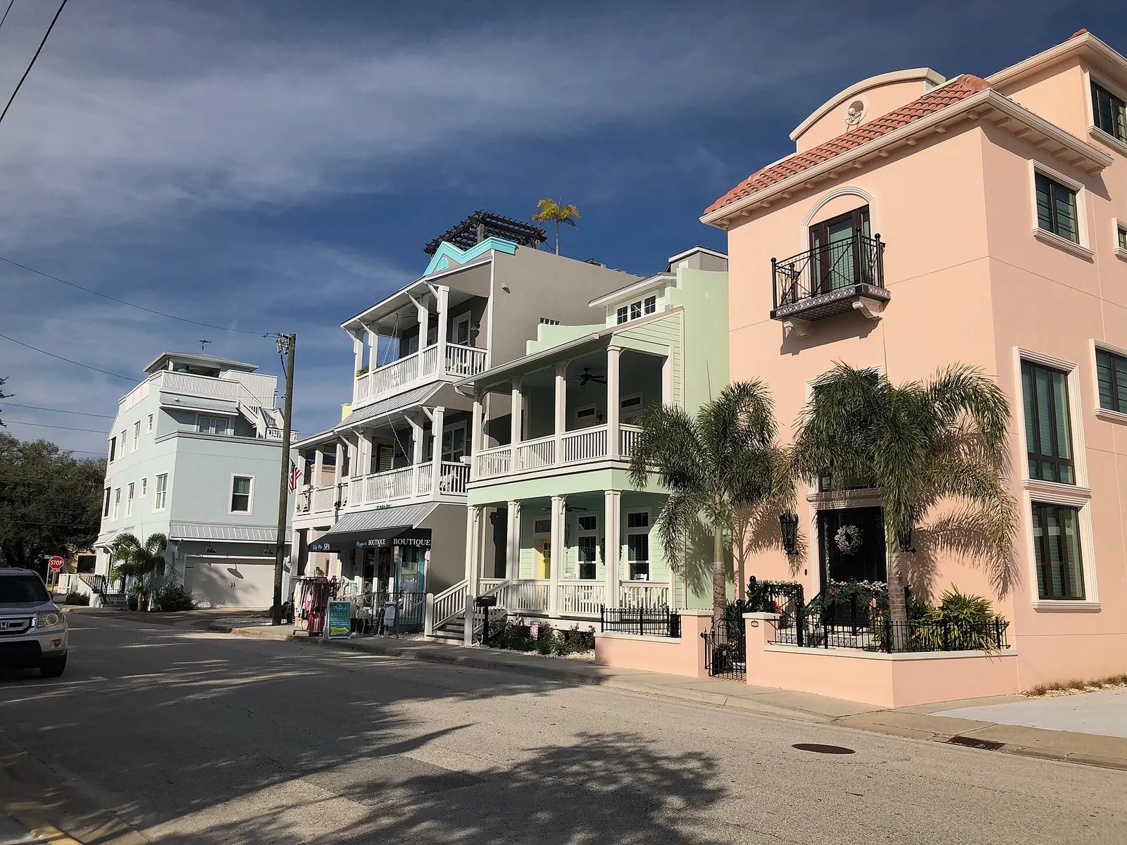 Row of pastel multi-storey buildings with porches and palms along a quiet street