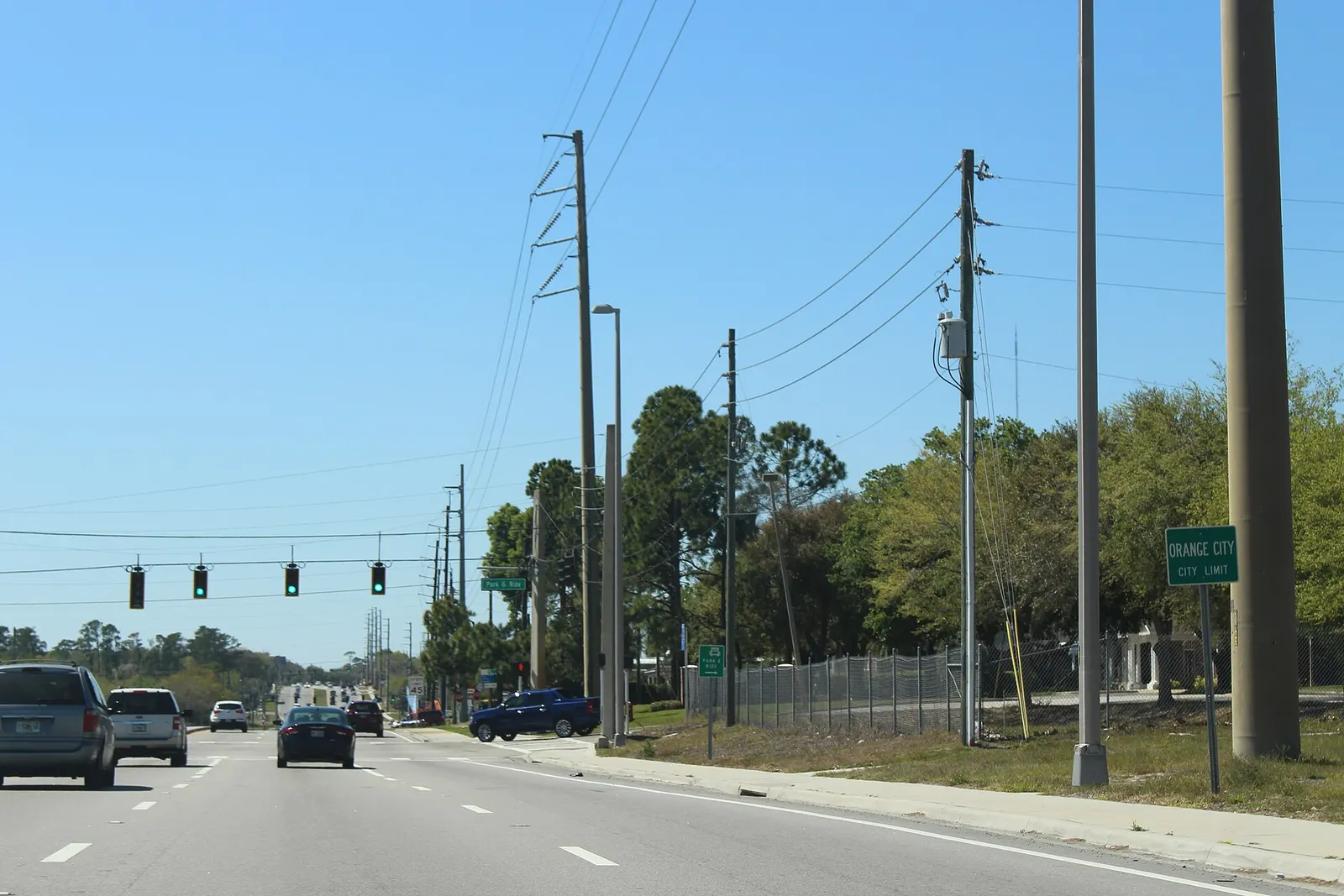 Westbound Saxon Boulevard with traffic, signals ahead and a green Orange City city limit sign on the roadside