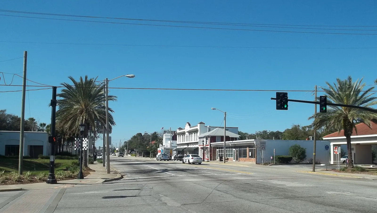 Granada Boulevard intersection with traffic signal, storefronts, palm trees and passing cars