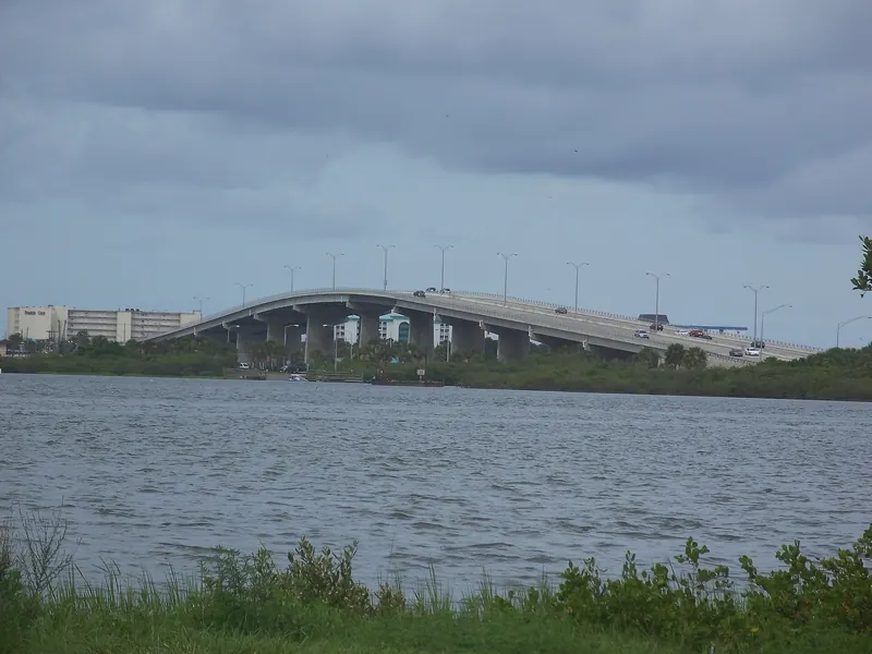 High-level Dunlawton Avenue bridge with cars crossing the Halifax River under grey clouds
