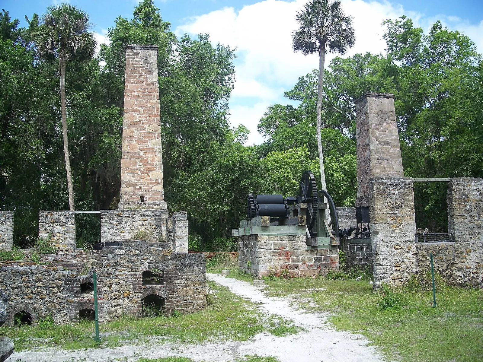 Stone sugar mill ruins with two chimneys and old iron machinery among trees