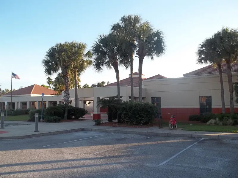 Low tan South Daytona City Hall building with tile roofs, tall palms and an empty parking lot